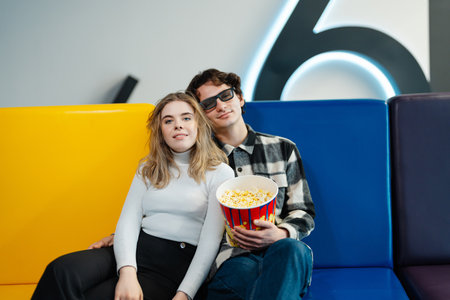 Couple enjoying popcorn while relaxing at a movie theater seating areaの写真素材