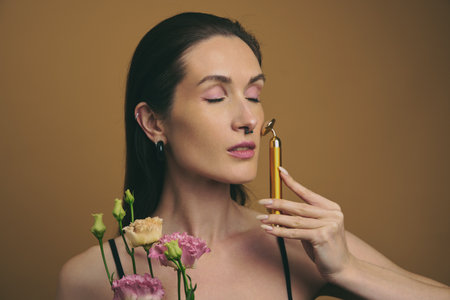 Woman holding flowers and facial tool on a warm backgroundの写真素材