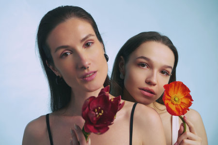 Two women holding flowers while posing against a light blue backgroundの写真素材
