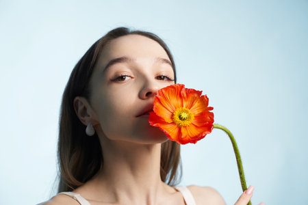 Woman holding vibrant orange flower close to her face in soft lightingの写真素材