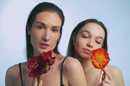 Two women holding vibrant flowers with soft, pastel backgroundの写真素材