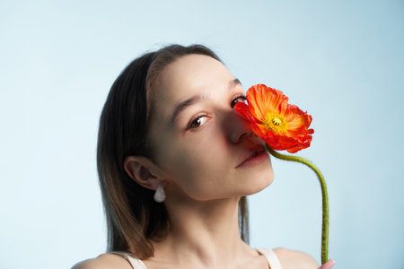Young woman holds bright orange flower near her face against a light backgroundの写真素材
