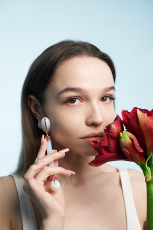 Woman holding red flower while using facial roller in studio settingの写真素材
