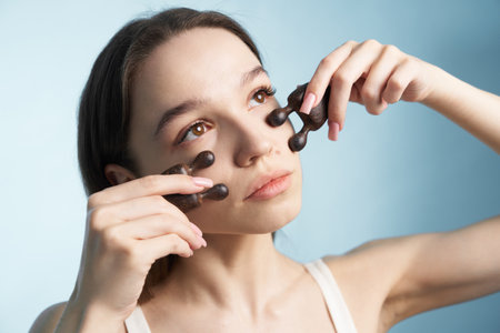 Woman applying facial roller for skincare routine in bright indoor spaceの写真素材