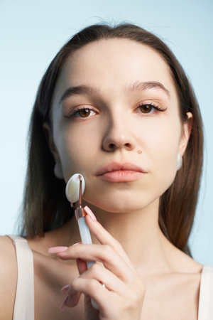 Young woman applying skincare using a jade roller in a bright spaceの写真素材