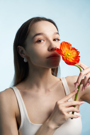 Woman holding a vibrant flower while posing against a light blue backgroundの写真素材