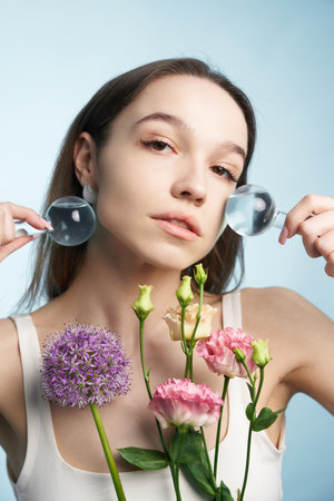 Young woman holds flowers and magnifying glasses in a studio settingの写真素材