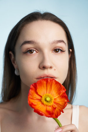 A woman with long hair poses holding an orange flower near her lipsの写真素材