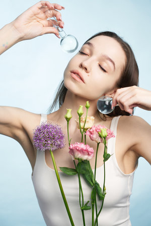 Young woman holding flowers and glass against light blue backgroundの写真素材