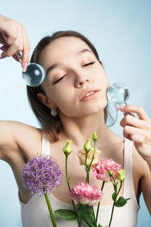 Woman applying beauty treatments with flowers against light blue backdrop