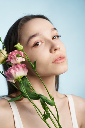 Young woman poses with delicate flowers against a soft blue backgroundの写真素材