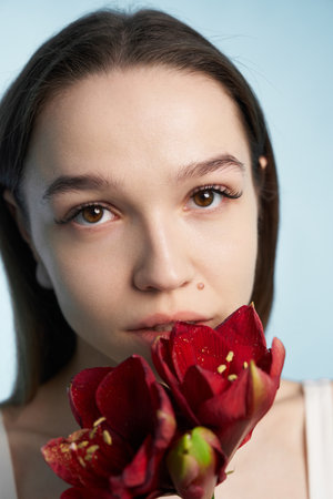 Young woman holding red flowers against a light blue backgroundの写真素材