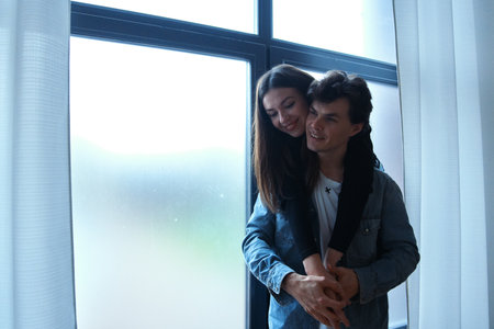 Couple enjoying cozy moments indoors by a large window on a cloudy dayの写真素材