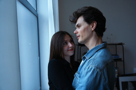 Couple embraces by a large window in a softly lit indoor space during evening