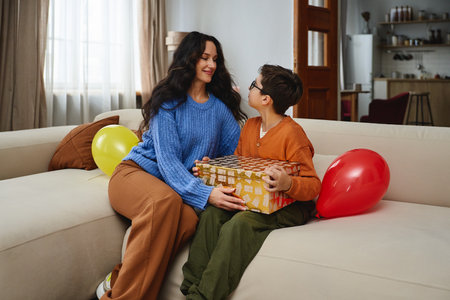 A woman and child celebrate with balloons and a gift in a cozy living roomの写真素材
