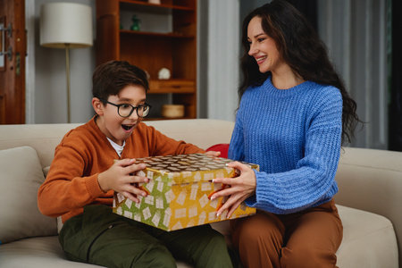 A young boy excitedly opens a colorful gift with his mom at homeの写真素材