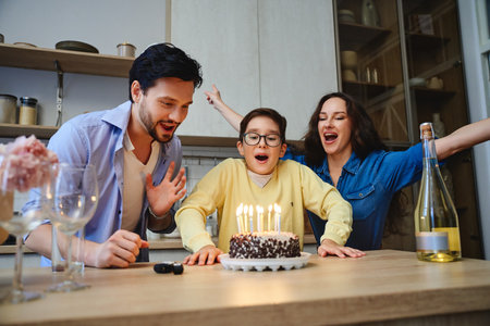 Family celebrates a childs birthday with a cake and candles in the kitchenの写真素材