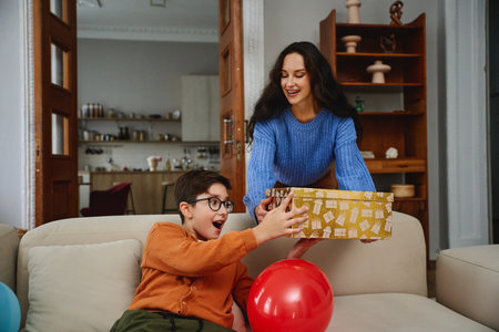 Joyful child receives a surprise gift from a smiling woman indoorsの写真素材