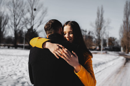 Couple embraces warmly in snowy park during winter afternoonの写真素材