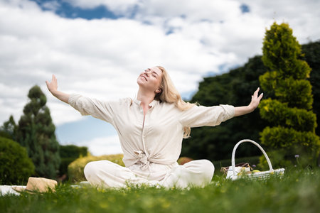 Joyful woman enjoying a sunny picnic in a lush green park under cloudsの写真素材
