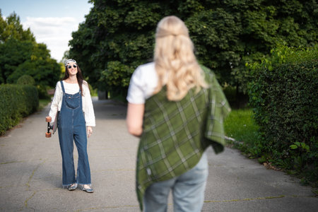 Two friends enjoying a sunny day in a park while wearing stylish outfitsの写真素材