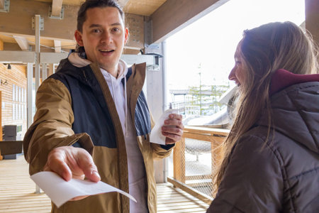 Excited brunette man visitor handing entrance ticket before accessing mountain observation attraction. Tourism service, admission control, travel experience and recreational destination concept.