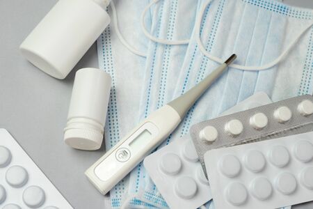 Pile of pills in blister packs, medical thermometer and mask on gray background. Disease prevention and treatment concept. Top view. Close up.の写真素材