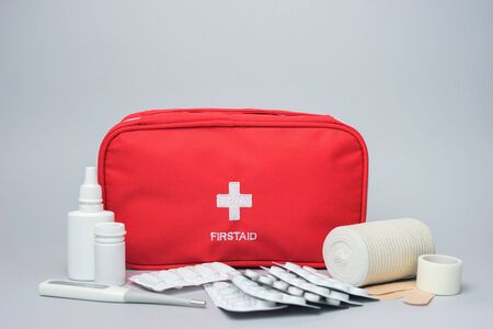 Medical first aid kit with medicine and pills. Isolated on gray background. Red bag with medical equipment and medications for emergency.の写真素材