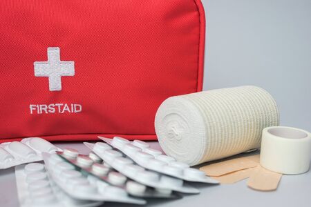 Medical first aid kit with medicine and pills on gray background. Red bag with medical equipment and medications for emergency. Top view. Close up.の写真素材