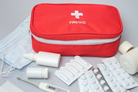 Medical first aid kit with medicine and pills on gray background. Red bag with medical equipment and medications for emergency. Top view.の写真素材