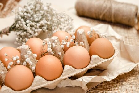 A tray of brown fresh hen's eggs decorated with flowers on wrinkled craft paper. Eeco-friendly egg production. Bakery ingredients. Organic chicken eggs. Eco Easter concept.の写真素材