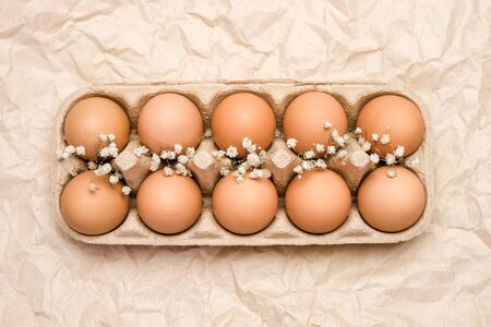 A tray of brown fresh hen's eggs decorated with flowers on wrinkled craft paper. Eeco-friendly egg production. Bakery ingredients. Organic chicken eggs - fresh from producer. Top view.の写真素材