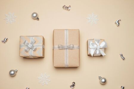 Gift boxes wrapped in kraft paper with white and silver ribbon and bow on pastel beige background. Winter holidays present concept. Christmas background, festive decor. Top view. Flat lay.の写真素材
