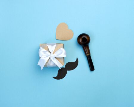 Happy fathers day composition. Gift box, black mustache, pipe and heart on blue background. Greeting card for dad. Top view flat lay.の写真素材