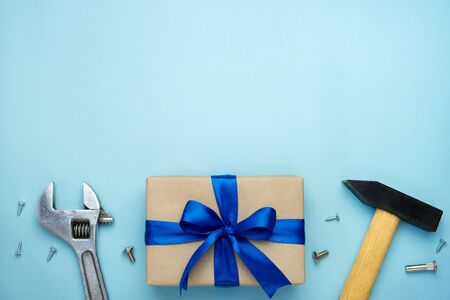 Fathers day composition. Gift box wrapped in kraft paper with blue ribbon bow and hand tools on blue background. Top view flat lay with free space for text. Greeting card for Mens day or Labor day.の写真素材