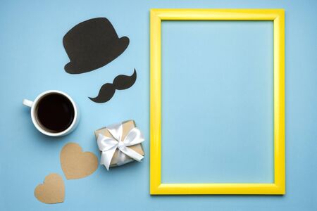 Fathers day composition with gift box, black mustache, hat, cup of coffe and heart on blue background. Copy space in yellow frame. Greeting card for dad. Top view flat lay.の写真素材