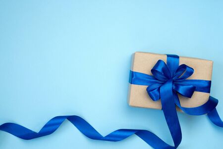 Gift box with blue ribbon bow isolated on blue background. Present for Fathers Day, Birthday or international Mens day Day. Festive decor background. Top view flat lay with free space.の写真素材