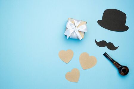 Father's day composition. Gift box with hearts and mustache, black hat and pipe on blue background. Top view flat lay with free space for text. Greeting card.の写真素材