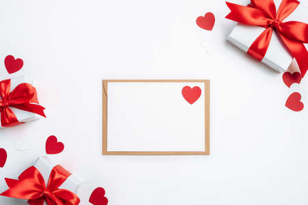 Gift boxes, envelope with blank card and red hearts on white background. Valentine day greeting card. Flat lay, top view.の写真素材