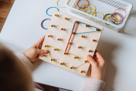Child is playing with wooden geoboard at home. Children's creative game for early development and fine motor skills.の写真素材