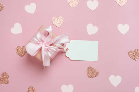 Gift box with blank gift tag on pastel pink background with many hearts. Valentines day composition. Top view, flat lay.の写真素材