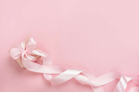 Gift box with long ribbon on pastel pink background. Present for Valentines Day, Mother's Day or Women's Day. Festive monochrome background. Top view flat lay with free space.の写真素材