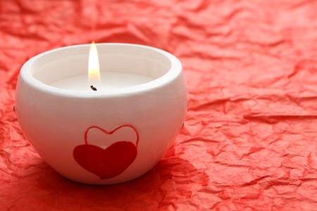 A burning white candle with hearts on it on the red backgroundの写真素材