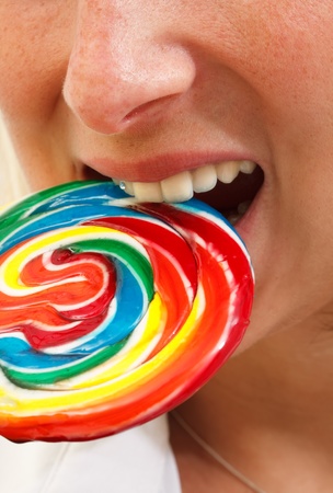 A young girl biting on a colorful spiral lollipopの写真素材