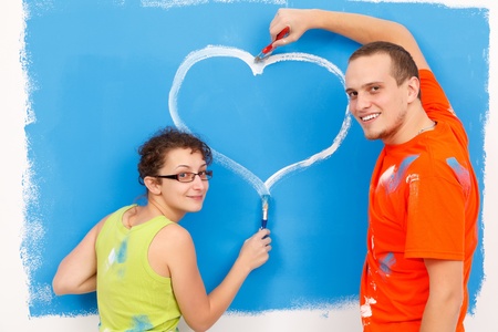 Young couple drawing a heart on the wall during home renovationの写真素材