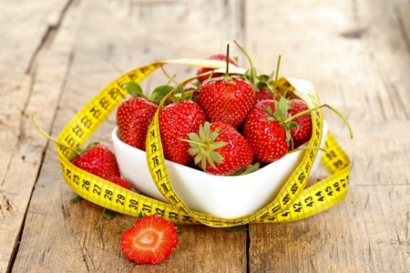 A bowl of fresh strawberries wrapped around with a measure tapeの写真素材