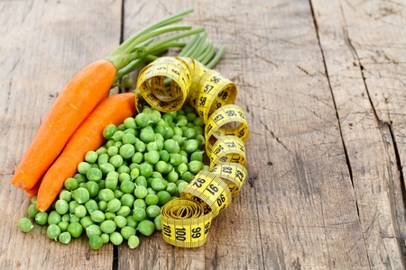 Carrots and peas with measure tape on wooden table, diet conceptの写真素材