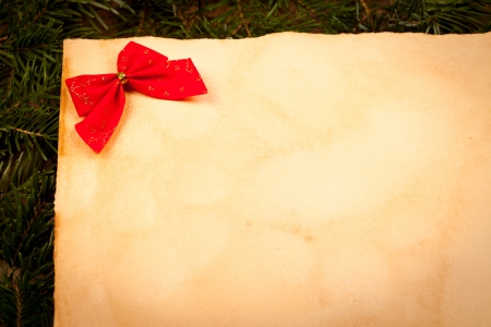 Red Christmas bow on old paper, green twigs in background.
の写真素材