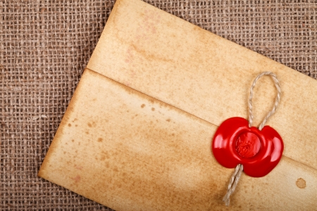 Detail of old grunge envelope with red wax seal on hessian sacking burlap background.
の写真素材