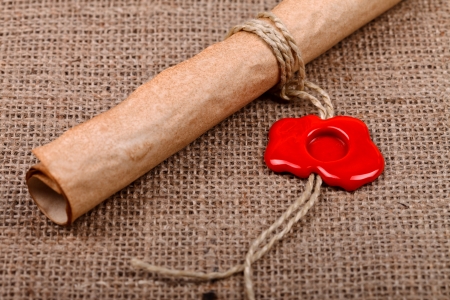 Old paper scroll with empty red wax seal on burlap .
の写真素材
